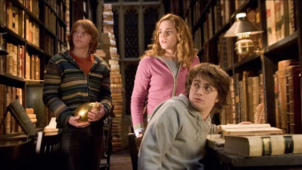 Cena do filme 'Harry Potter', com os três protagonistas na biblioteca