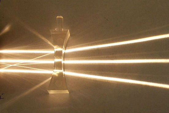 Nas lentes divergentes, os raios de luz paralelos entre si que incidem sobre a lente são refratados em direções diferentes, que acabam divergindo em um mesmo ponto. (Imagem: Wikimedia Commons)