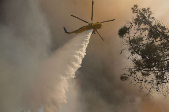 Um helicóptero dos bombeiros é utilizado para jogar água sobre as chamas da região de Lower Lake, na Califórnia. (Imagem: Getty Images)