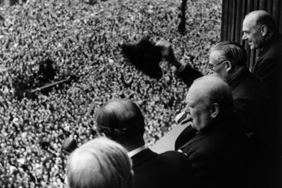 O Primeiro Ministro da Inglaterra Winston Churchill acena para a multidão reunida em frente ao Palácio Whitehall no dia 8 de maio de 1945, o Dia da Vitória na Europa. (Créditos: Keystone/Getty Images)
