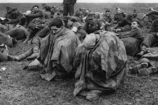 Cansados e desolados, prisioneiros de guerra alemães se abrigam debaixo de capas impermeáveis após serem capturados nas margens do rio Reno. (Créditos: Fred Ramage/Keystone/Getty Images)