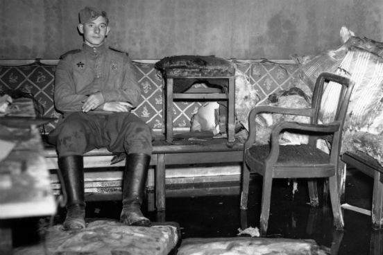 Um soldado russo senta-se sobre o sofá onde se acredita que Adolf Hitler se suicidou em seu abrigo subterrâneo, o Führerbunker, em Berlim. (Foto: Fred Ramage / Keystone / Getty Images)