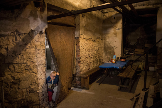 As crianças Pavel Makeev, de cinco anos de idade, e Raya Makeeva, de sete, esperam o almoço ficar pronto no porão de um centro cultural no leste da Ucrânia, onde vivem atualmente. A região tem sido fortemente atacada por forças ucranianas, obrigando a maioria dos moradores a fugir ou a se esconder em lugares como esse. As pessoas têm vivido no espaço desde junho de 2014. (Foto: Andrew Burton / Getty Images)
