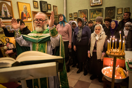 Grupo se reúne para orações em escritório de igreja ortodoxa russa em Donetsk, na Ucrânia. O salão principal da igreja foi destruído por um bombardeio em 2014, forçando a congregação a se reunir em um espaço improvisado desde então. (Foto: Andrew Burton / Getty Images).
