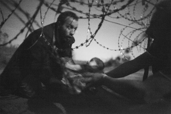 A grande vencedora deste ano na premiação da WWP é esta imagem que mostra um homem passando um bebê para uma outra pessoa por baixo de uma cerca de arame farpado. A foto foi registrada pelo australiano Warren Richardson no dia 28 de agosto de 2015, na fronteira entre a Sérvia e a Hungria. Segundo o fotógrafo, que acampou com os refugiados, essas pessoas tentavam chegar na Hungria antes que a cerca de segurança estivesse concluída (Crédito foto: Warren Richardson/World Press Photo 2016). A grande vencedora deste ano na premiação da WWP é esta imagem que mostra um homem passando um bebê para uma outra pessoa por baixo de uma cerca de arame farpado. A foto foi registrada pelo australiano Warren Richardson no dia 28 de agosto de 2015, na fronteira entre a Sérvia e a Hungria. Segundo o fotógrafo, que acampou com os refugiados, essas pessoas tentavam chegar na Hungria antes que a cerca de segurança estivesse concluída (Crédito foto: Warren Richardson/World Press Photo 2016).