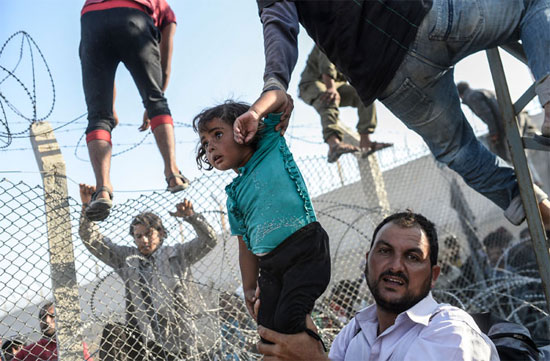 Refugiado sírio segura uma garota, enquanto outras pessoas tentam escalar a cerca de segurança para chegar até o campo de refugiados em Akçakale, na Turquia. Desde que o conflito na Síria começou, em 2011, quase 2 milhões de sírios fugiram para a Turquia (Crédito foto: Bulent Kilic/Agence France Presse).
