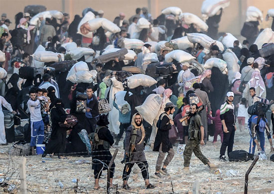 A imagem mostra, em primeiro plano, membros do grupo extremista Estado Islâmico conduzindo dezenas de sírios de volta para as suas cidades. Essas pessoas tentavam cruzar a fronteira com a Turquia para chegar ao campo de refugiados em Akçakale, mas foram impedidas pelos terroristas (Crédito foto: Bulent Kilic/Agence France Presse).
