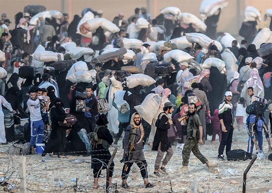 A imagem mostra, em primeiro plano, membros do grupo extremista Estado Islâmico conduzindo dezenas de sírios de volta para as suas cidades. Essas pessoas tentavam cruzar a fronteira com a Turquia para chegar ao campo de refugiados em Akçakale, mas foram impedidas pelos terroristas (Crédito foto: Bulent Kilic/Agence France Presse). A imagem mostra, em primeiro plano, membros do grupo extremista Estado Islâmico conduzindo dezenas de sírios de volta para as suas cidades. Essas pessoas tentavam cruzar a fronteira com a Turquia para chegar ao campo de refugiados em Akçakale, mas foram impedidas pelos terroristas (Crédito foto: Bulent Kilic/Agence France Presse).