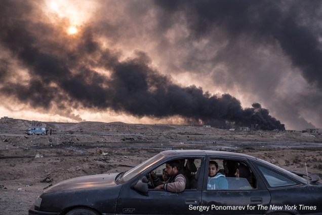 Família foge de Mossul, a segunda maior cidade do Iraque, enquanto campos de petróleo queimam ao fundo, em novembro de 2016. A cidade, ocupada pelo grupo terrorista Estado Islâmico, é alvo de operações das forças iraquianas para tentar retomar o controle.
<div class="photo-desc"><span>(foto: Sergey Ponomarev/World Press Pohto 2017)</span></div>
