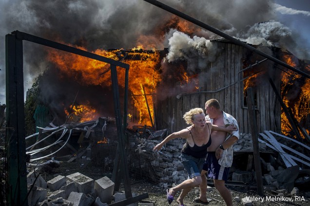 Civis fogem de uma casa em chamas, destruída após um ataque aéreo na região de Donbass, na Ucrânia, em julho de 2014. No período, o leste do país era palco de confrontos entre separatistas, apoiados pela Rússia, e as forças da Ucrânia.

<span>(foto Valery Melnikov/World Press Photo 2017)</span>