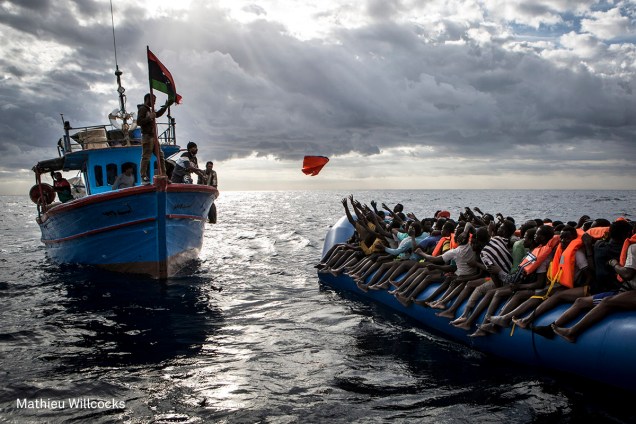 Pescador líbio joga um colete salva-vidas em direção a um bote inflável lotado de imigrantes, no Mar Mediterrâneo, em novembro de 2016.

(foto: Mathieu Willcocks/World Press Photo)