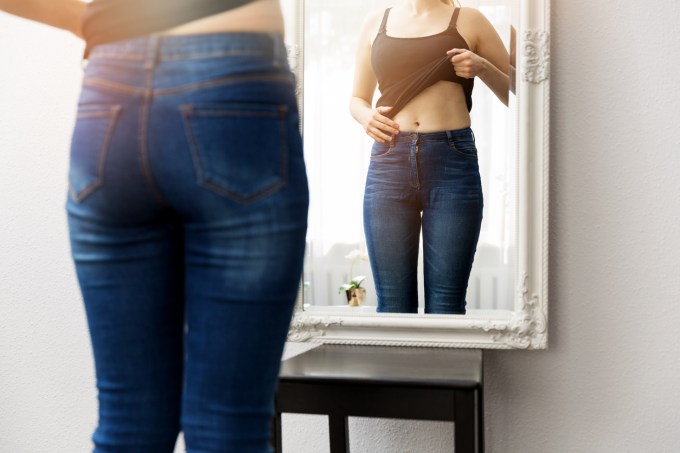 Mulher observando o próprio corpo em frente ao espelho
