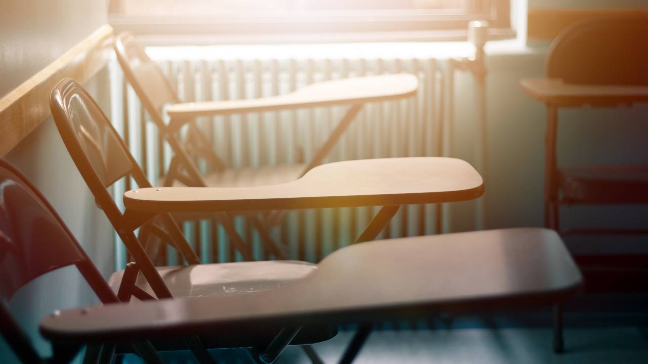 Três cadeiras enfileiradas no fundo de uma sala de aula