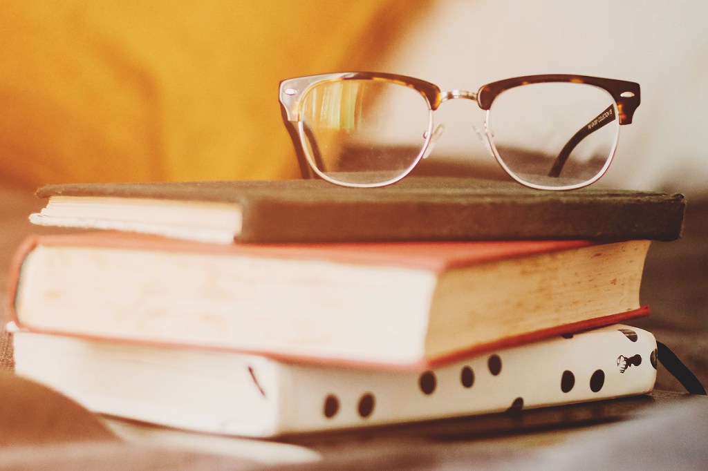 pilha de livros com um óculos em cima