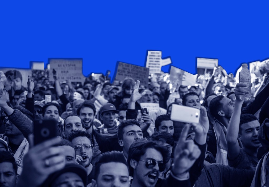 Multidão em protesto, em frente a um fundo azul.