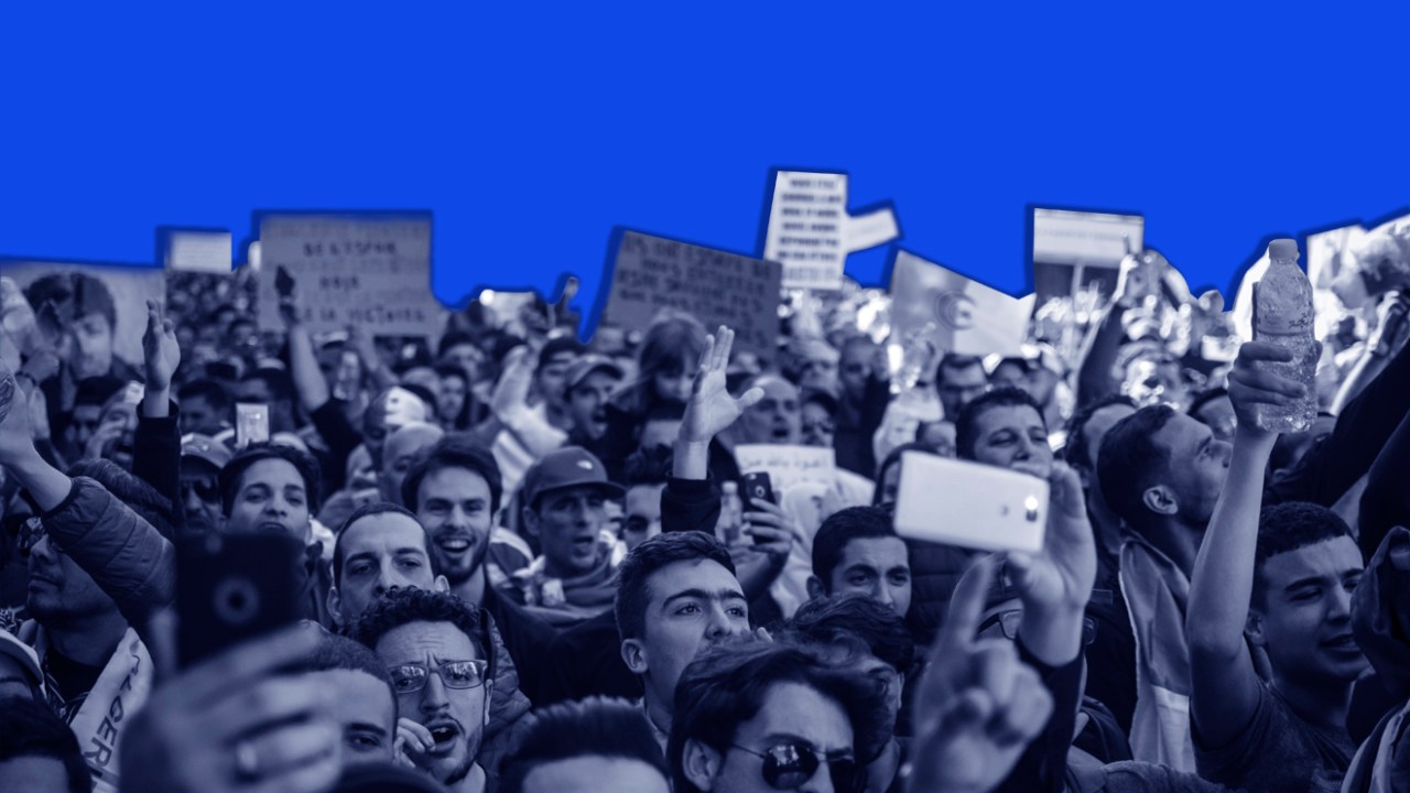 Multidão em protesto, em frente a um fundo azul.