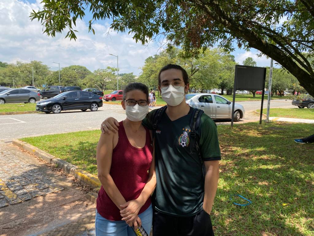 FUVEST Andrew Mãe e filho se abraçam na sombra, ambos de máscara.