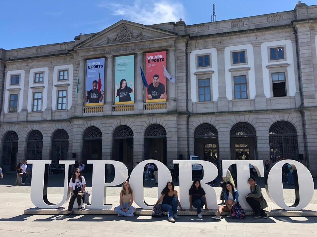 Jovens posam no letreiro da Universidade do Porto, em frente a um dos prédios principais da instituição.