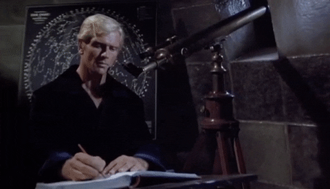Homem sentando escreve um livro numa mesa, enquanto observa com os olhos em um telescópio antigo. Ele usa roupas pretas e parece estar em um ambiente feito de paredes de pedra. Atrás dele, há um quadro negro com um mapa de algumas constelações.
