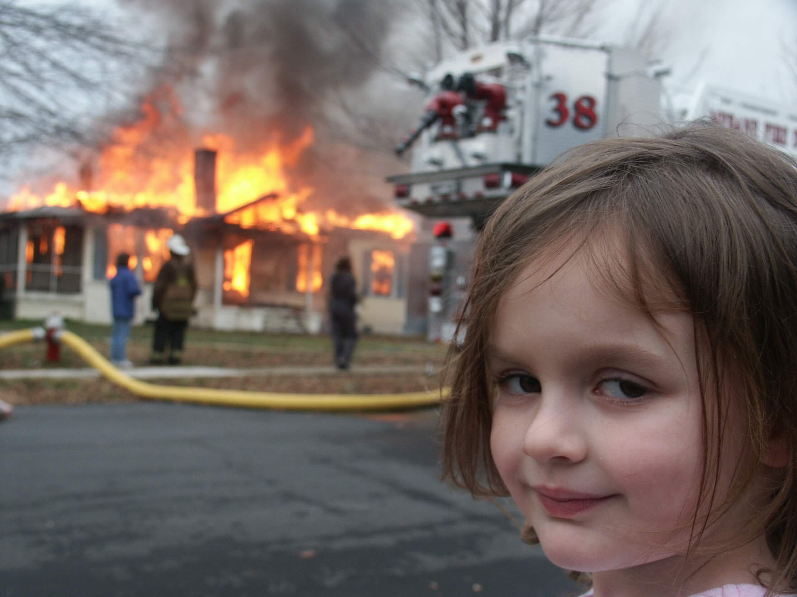 Menina olha diretamente para a câmera com olhar maléfico enquanto uma casa em chamas é socorrida pelos bombeiros.