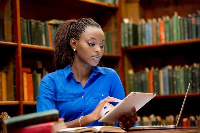 Jovem estuda com tablet e notebook em uma biblioteca