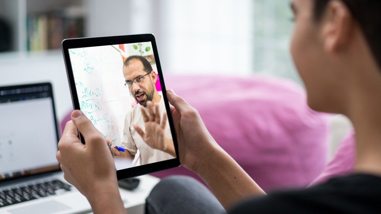 Estudante em uma aula online ouve os ensinamentos de um professor por meio de um tablet