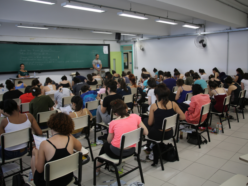 Vários estudantes numa sala de aula fazendo a prova do vestibular.
