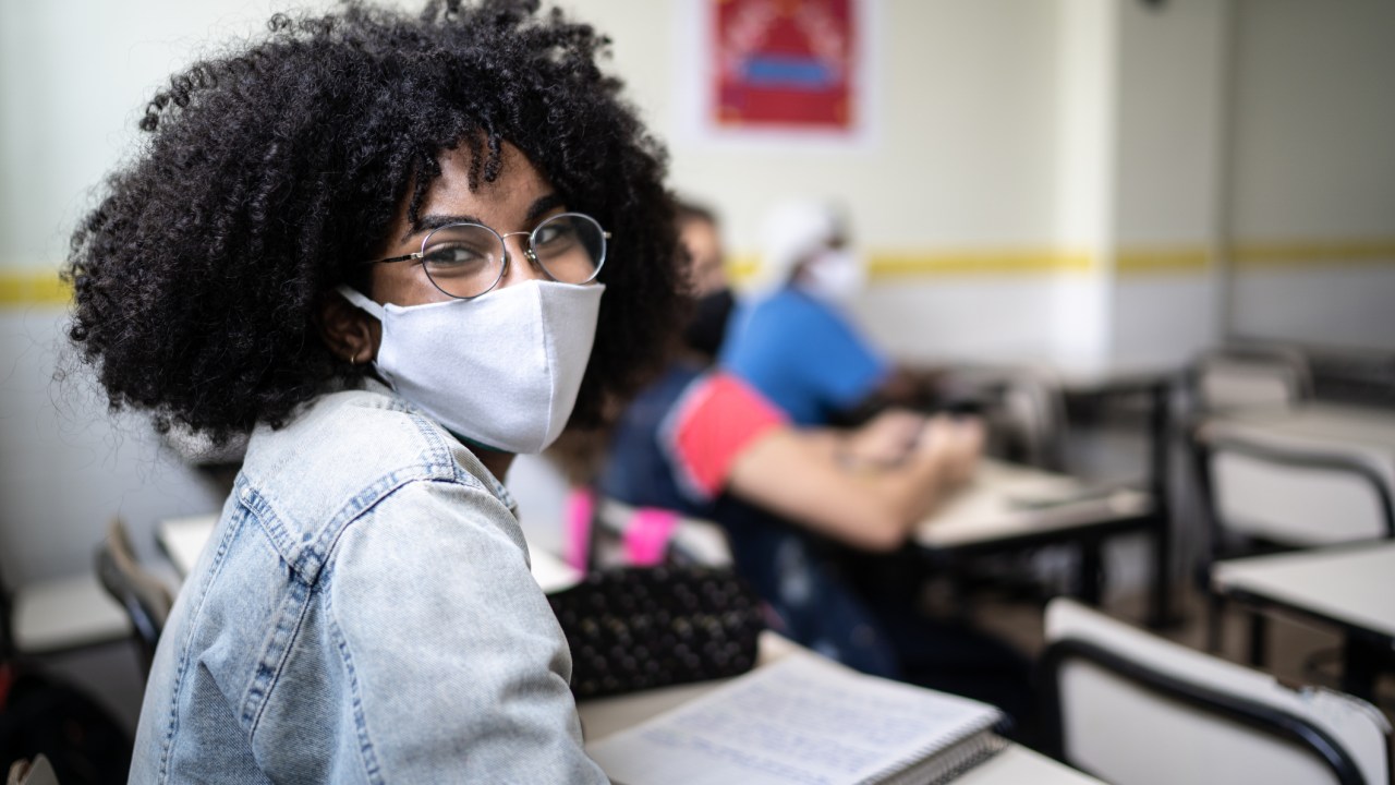 Estudante negra usa máscara e jaqueta jeans em uma sala de aula