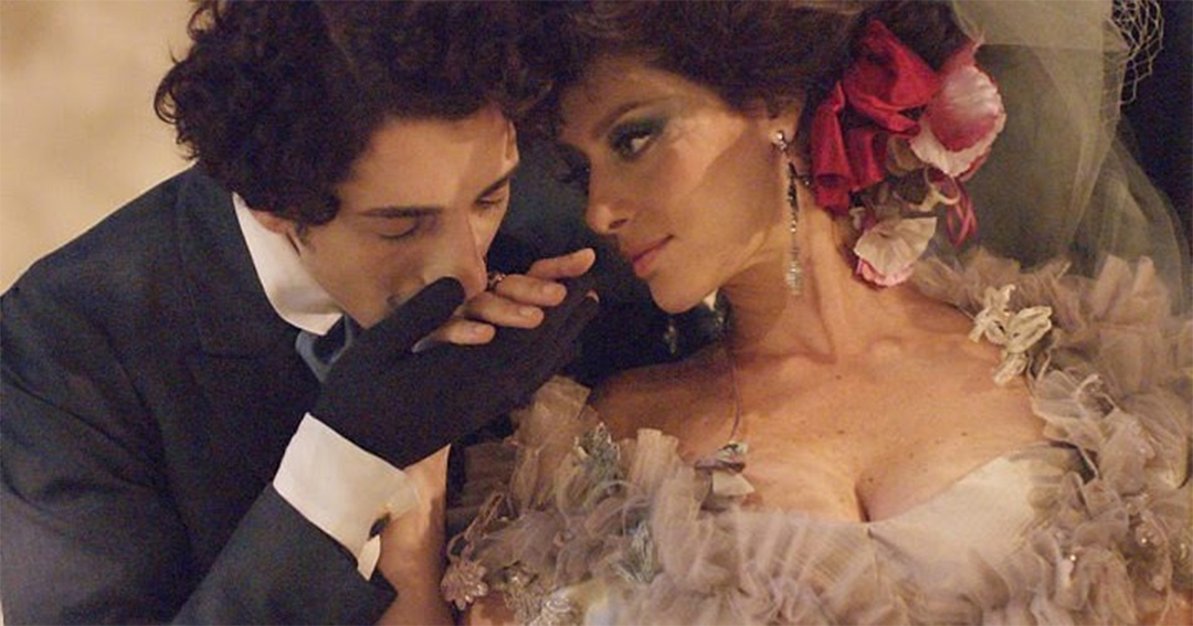 Cena da minissérie Capitu, de 2008, com atores interpretando Bentinho e Capitu. Bentinho está beijando a mão de Capitu, que está de lado para ele.