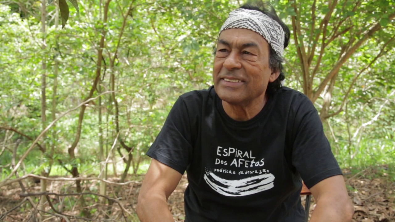 Ailton Krenak é um homem indígena na casa dos 70 anos, ele está usando uma camisea preta e uma faixa na cabeça