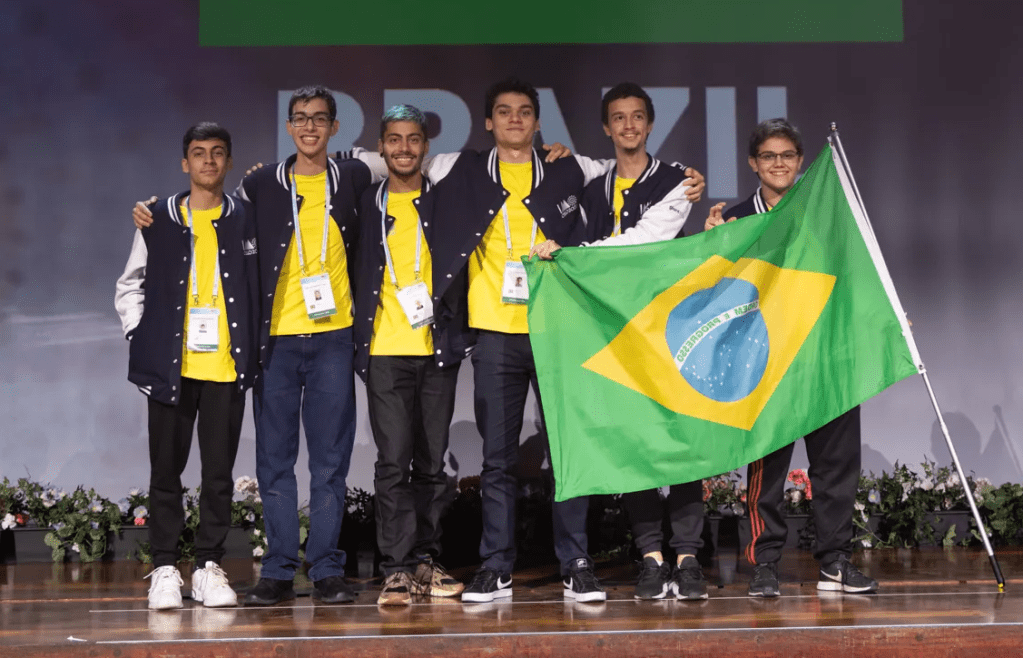 Equipe brasileira da IMO 2022: são seis jovens rapazes segurando a bandeira do Brasil em um palco.