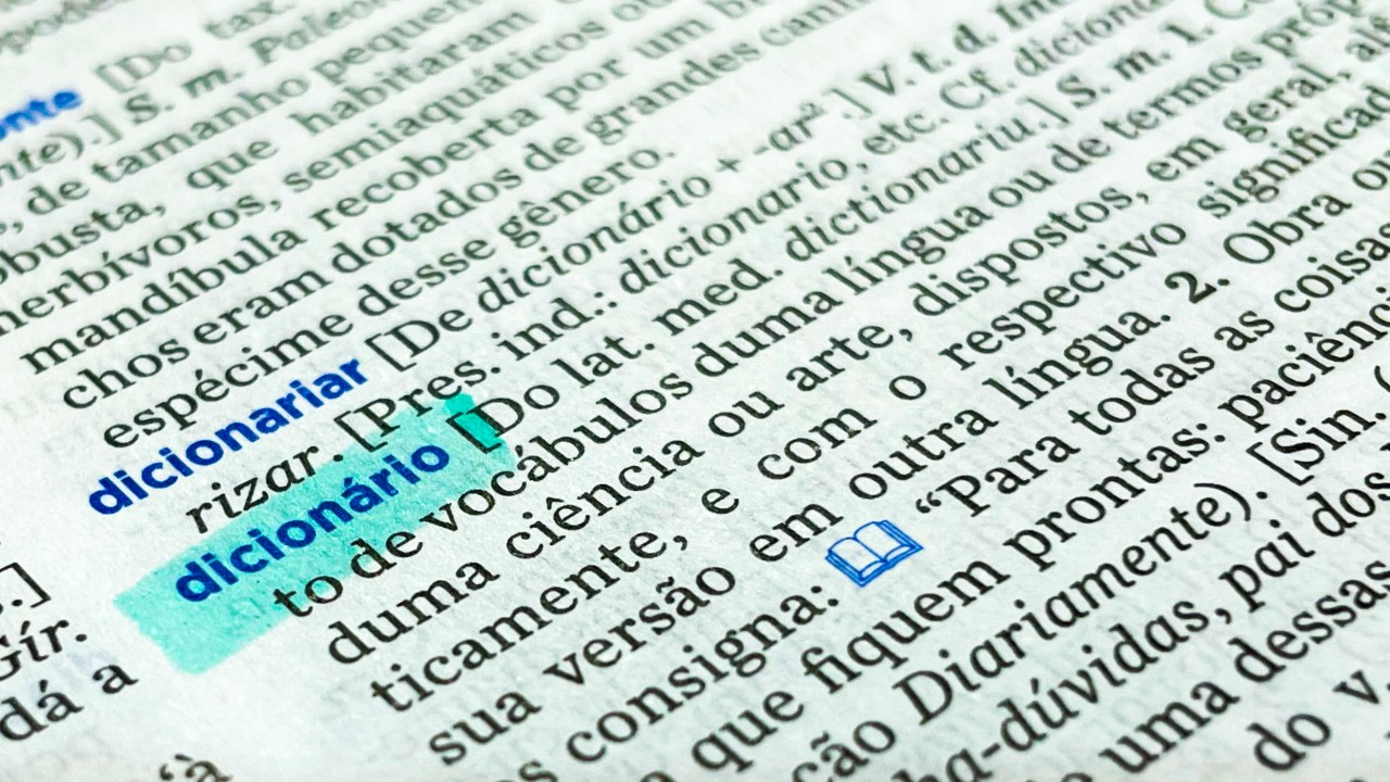Dicionário aberto, com a definição da palavra "dicionário" grifada.