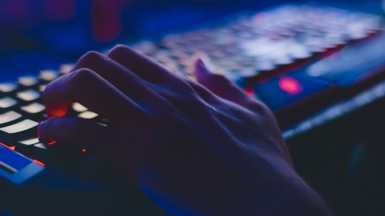 Imagem focada em uma mão em um teclado, com teclas iluminadas