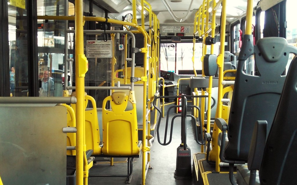 Parte de interna de um ônibus público: bancos, uma catraca e barras de apoio