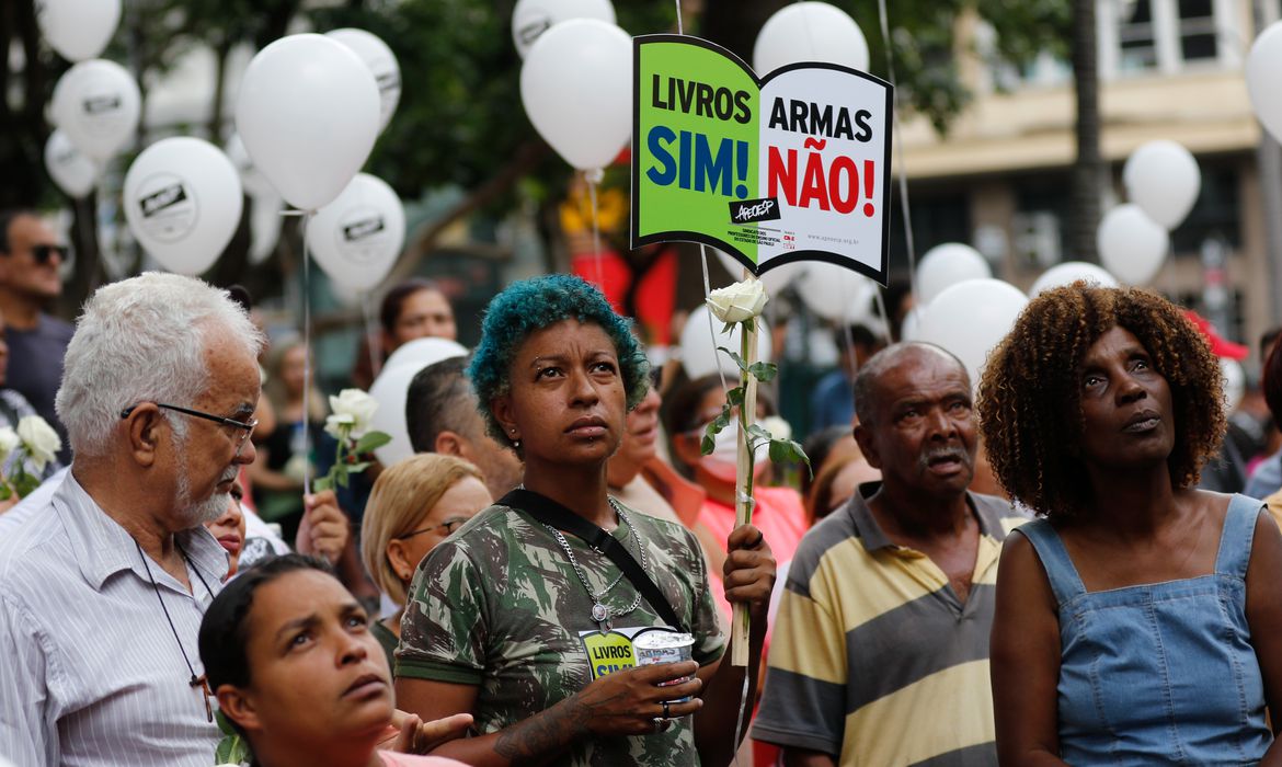 professores protestam contra violência nas escolas. Uma delas, mulher negra de cabelos curtos, carrega uma placa escrito "livros sim, armas não".