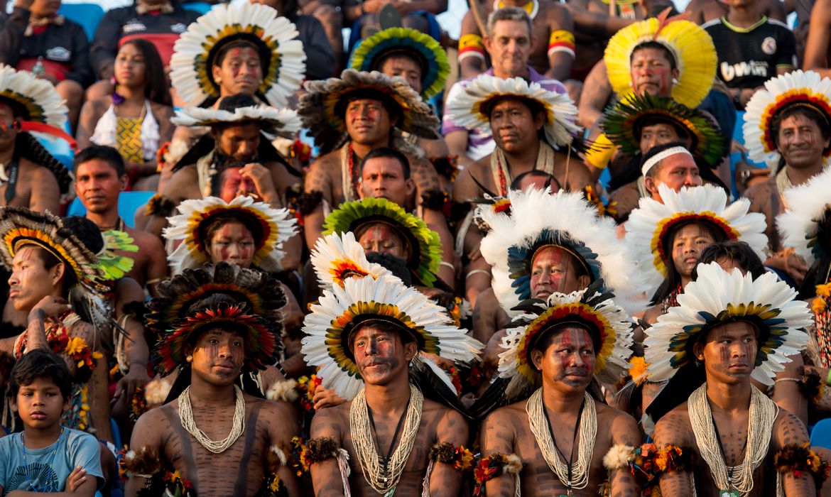 Vários indígenas usando cocares brancos assistem a um jogo