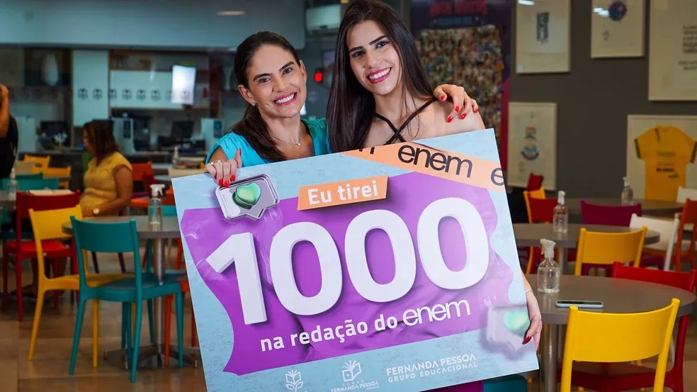 A professora Fernanda Pessoa e a estudante Carina Moura, as duas seguram juntas um cartaz escrito 