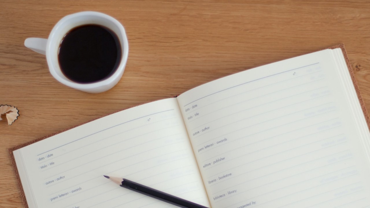 Mesa; estudos; caderno; café; xícara de café ao lado de caderno e lápis preto
