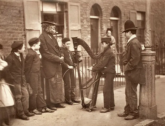 Jovens na rua de Londres de 1870 tocam uma harpa.