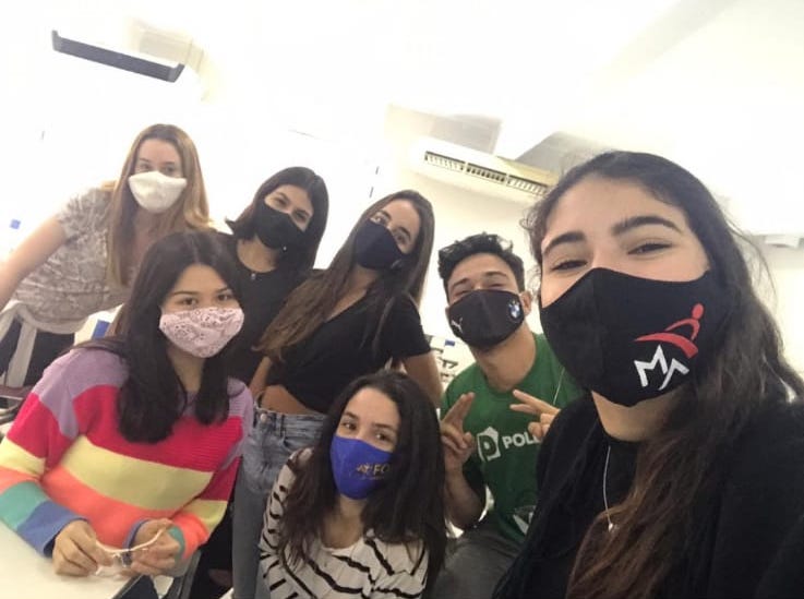 Lyncoln ao lado de amigas em uma sala de aula, todos usam máscara