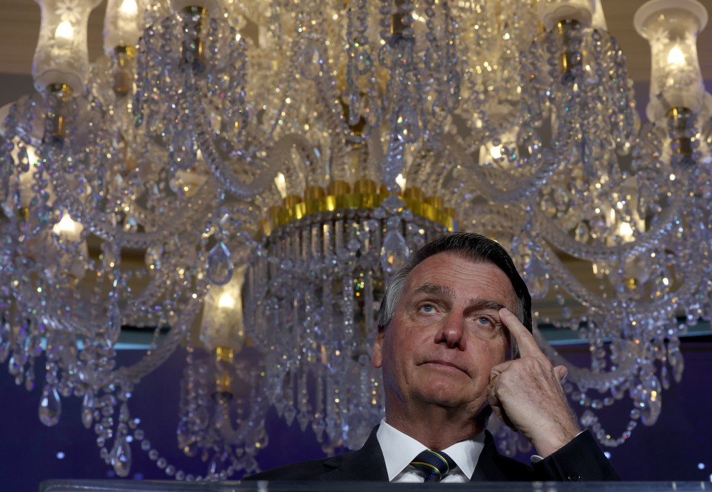 o ex-presidente Jair Bolsonaro, com a mão na sobrancelha, em frente a um lustre luxuoso