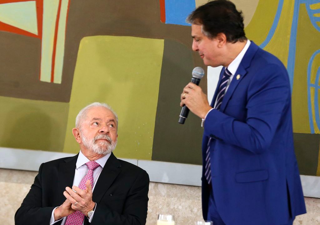 Lula sentado olha para o ministro da Educação, Camilo Santana
