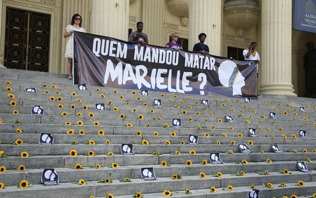 protesto pela apuração do assassinato de Marielle Franco em escadaria. Mulheres seguram cartaz questionando 