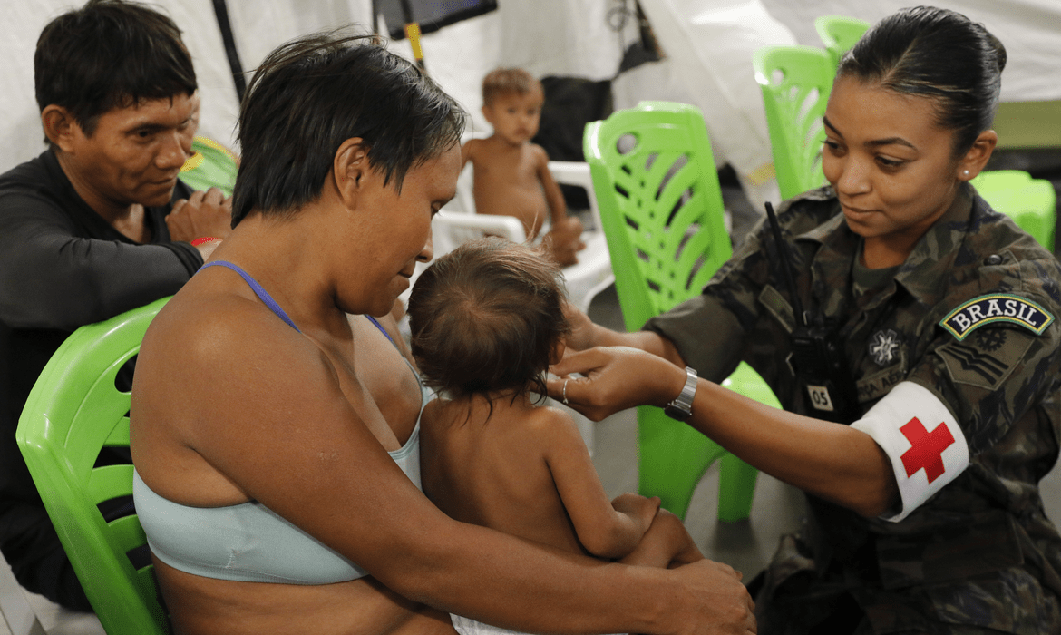 Mãe e criança yanomami são atendidas por agente de saúde.