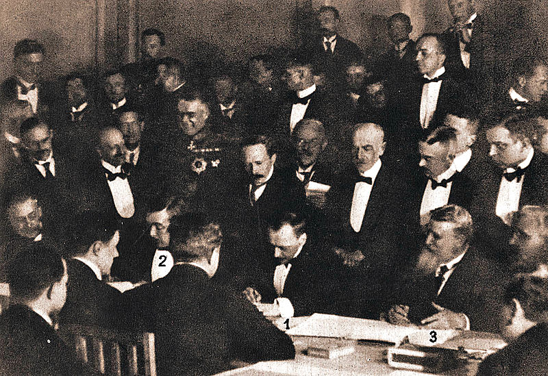 homens reunidos em uma sala, vestindo smoking, para assinatura de um tratado de paz para a primeira guerra mundial