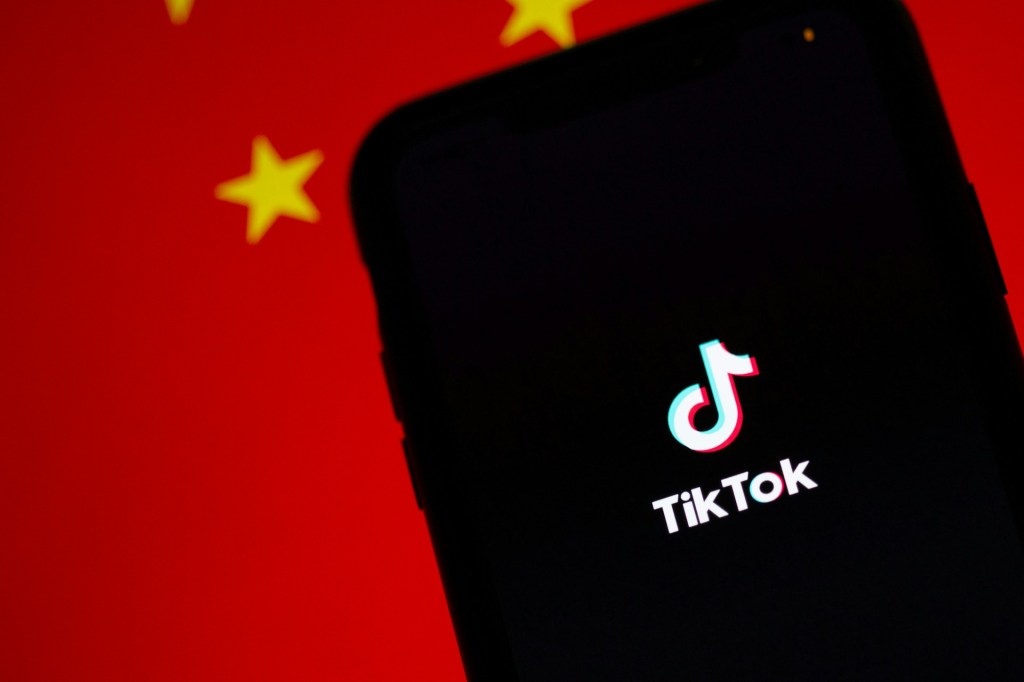 Celular com aplicativo do TikTok aberto, com a bandeira da China ao fundo.
