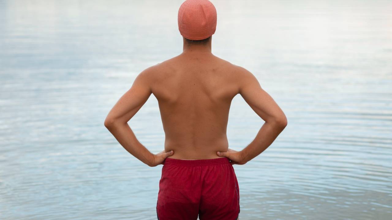 Homem em pé, de costas, só de sunga, prestes a entrar em psicina