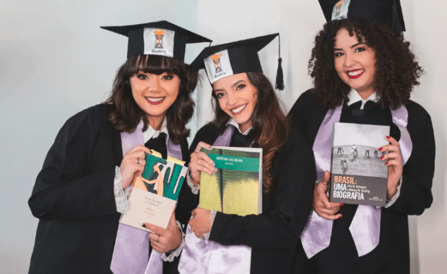 Débora Aladim de beca, ao lado de duas colegas de faculdade.