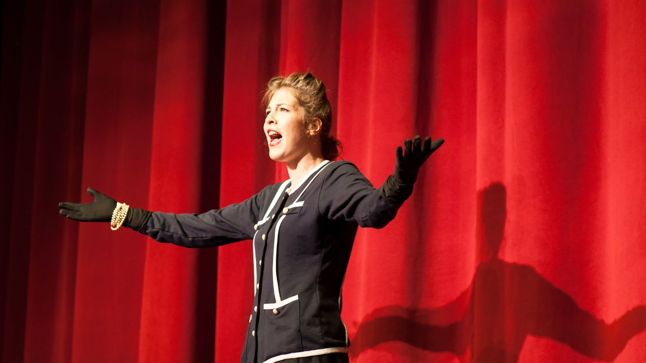 Mulher atuando em frente às cortinas vermelhas de um teatro