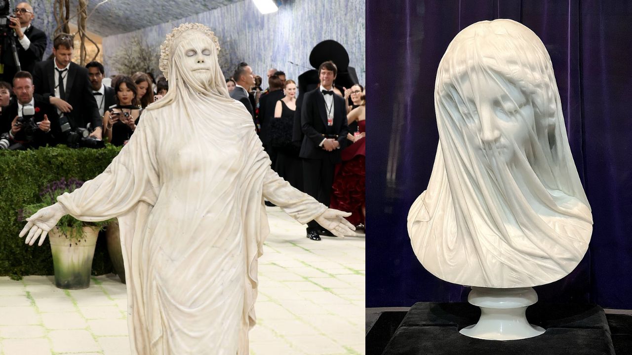 Uma pessoa vestida com um traje branco esvoaçante, que lembra uma estátua de mármore com véu, posa com confiança em um evento formal, cercada por fotógrafos. Um busto de mármore semelhante é exibido à direita. A atmosfera é artística e dramática.